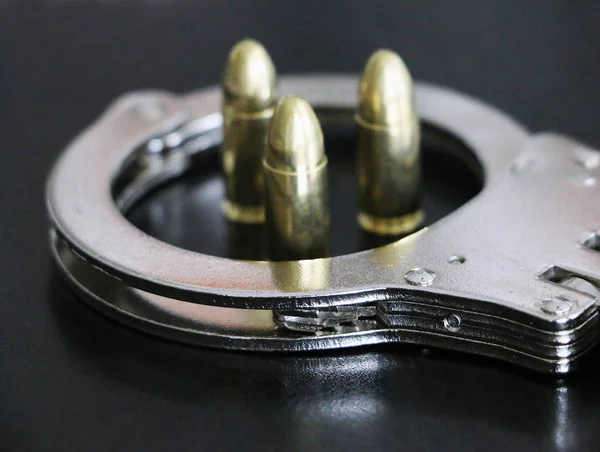 Handschellen und Pistolenkugeln auf schwarzem Hintergrund — Stockfoto