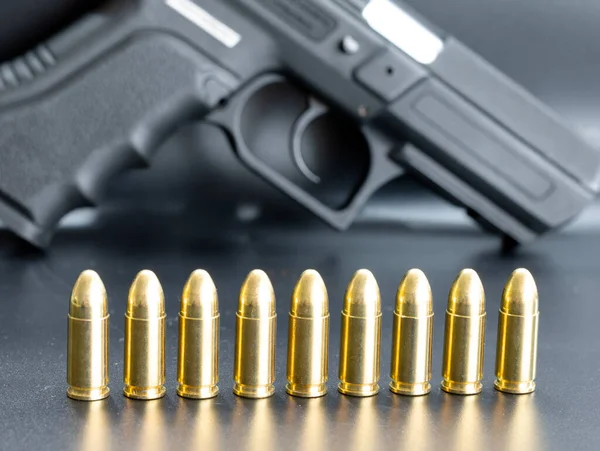 Row of 9 mm pistol bullets on dark background with gun