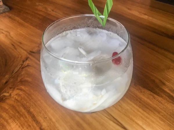 Glass of fresh coconut juice, drink coconut water naturally cool. Indonesian Ice coconut drink or kelapa muda on glass with leaf in isolated wooden background