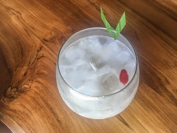 Glass of fresh coconut juice, drink coconut water naturally cool. Indonesian Ice coconut drink or kelapa muda on glass with leaf in isolated wooden background