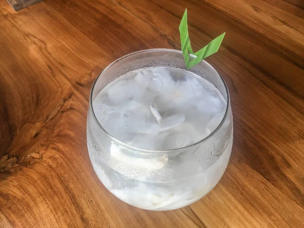 Glass of fresh coconut juice, drink coconut water naturally cool. Indonesian Ice coconut drink or kelapa muda on glass with leaf in isolated wooden background