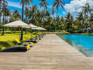Şemsiyeli otel veya tatil beldesinde güzel tropikal yüzme havuzu, hindistan cevizi ağacı şezlongları, sonsuzluk havuzu manzaralı palmiye ağaçları, okyanus ve dağ arka planı