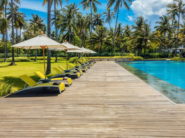 Beautiful tropical swimming pool in hotel or resort with umbrella, coconuts tree sun-loungers, palm trees with infinity pool view, ocean and mountain background