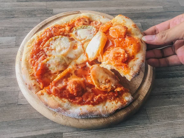 Taking a slice of pizza in pan isolated in wood background