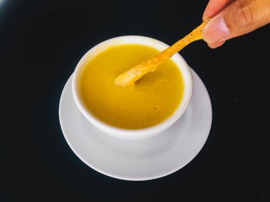kaşıkla el siyah arka plan üzerinde izole beyaz bir kapta Saf sarı kremsi Mısır çorbası almak. Sağlıklı gıda