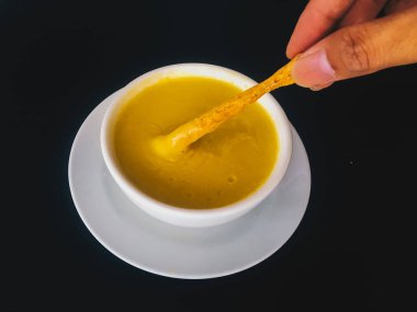 kaşıkla el siyah arka plan üzerinde izole beyaz bir kapta Saf sarı kremsi Mısır çorbası almak. Sağlıklı gıda