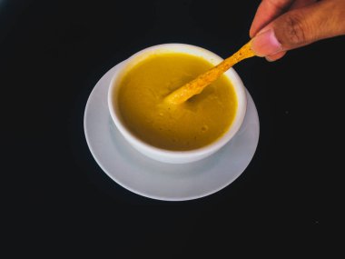 kaşıkla el siyah arka plan üzerinde izole beyaz bir kapta Saf sarı kremsi Mısır çorbası almak. Sağlıklı gıda