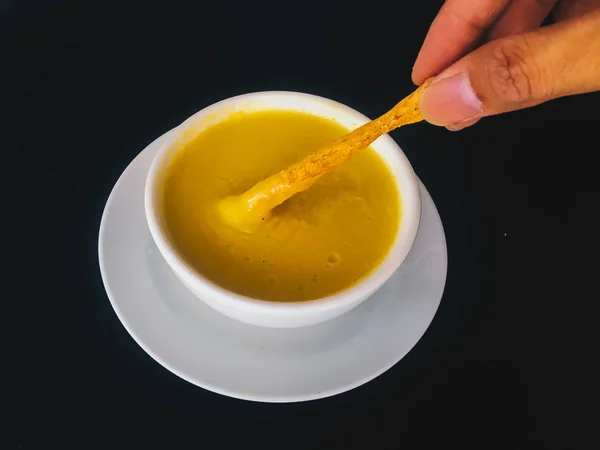 hand with spoon take Pure yellow creamy Corn soup with in a white bowl isolated on black background. Healthy food