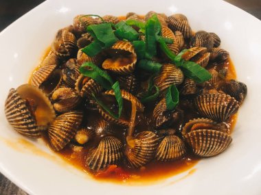 Izgara cockles veya lezzetli bir kırmızı sos ve üzerinde frenk soğanı ile istiridye. beyaz bir tabak üzerinde buğulanmış istiridye