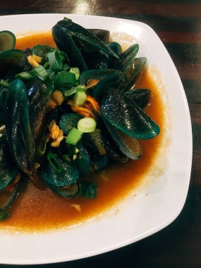 Lezzetli bir kırmızı sos ve üzerinde frenk soğanı ile ızgara midye. beyaz bir tabak üzerinde buğulanmış istiridye