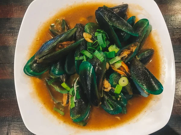 Lezzetli bir kırmızı sos ve üzerinde frenk soğanı ile ızgara midye. beyaz bir tabak üzerinde buğulanmış istiridye