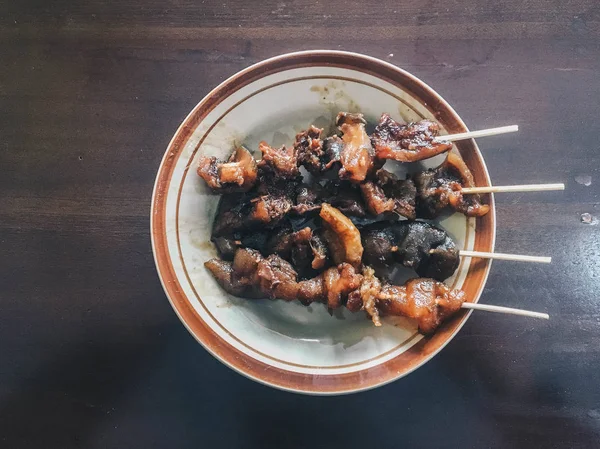 カンビング ゴレンまたはヤギのサテは 木製のテーブルの上にスライスされたシャロットとチリとピーナッツソースを混ぜた羊肉から作られた伝統的なインドネシア料理です — ストック写真