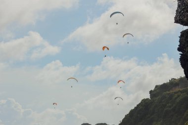 Bali sahilinde yamaç paraşütü, Endonezya. Parlak güneşli bir günde plaj, uçurum, mavi su ile deniz üzerinde uçan Yamaç paraşütü tandem
