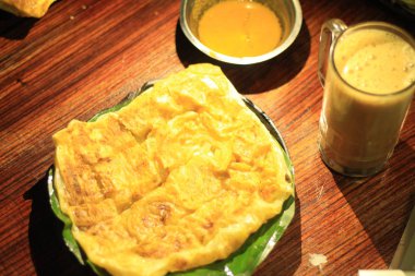 Roti Canai veya Canai Ekmek veya Parata Ekmek veya prata Ekmek tarık çay veya spot altında koyu arka plan ile ahşap arka plan üzerinde izole muz yaprağı plaka üzerinde tarık ve köri sosu