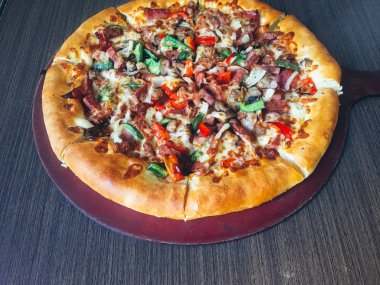 koyu masada servis edilen et ve sebze ile dilimlenmiş pizza