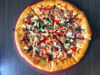 koyu masada servis edilen et ve sebze ile dilimlenmiş pizza