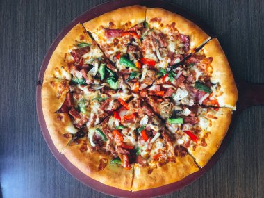 koyu masada servis edilen et ve sebze ile dilimlenmiş pizza