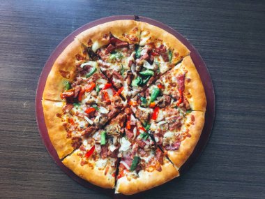 koyu masada servis edilen et ve sebze ile dilimlenmiş pizza