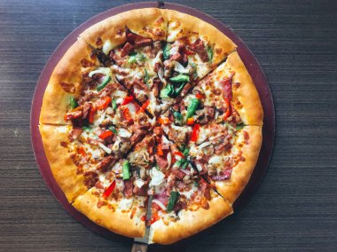 koyu masada servis edilen et ve sebze ile dilimlenmiş pizza