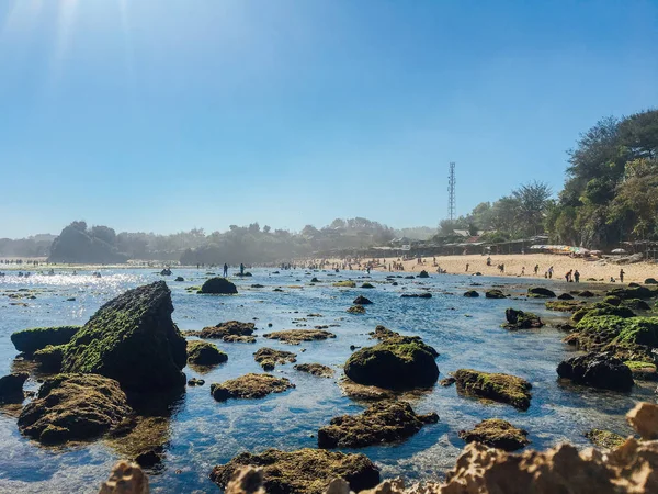 美丽的海滩在古农基杜尔 印度尼西亚白天与人 珊瑚岩石 绿色海藻 和低潮在前景 — 图库照片