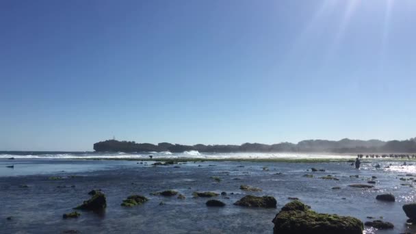 Belle plage à Gunung Kidul, Indonésie à la lumière du jour avec des gens, rocher de corail, algues vertes, et marée basse au premier plan 
