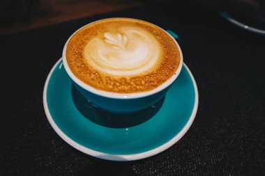 Kahve Latte veya Cappuccino köpüklü bir fincan, kafede siyah masada yeşil kahve fincanı