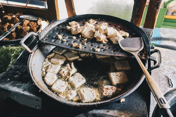 White tofu cubes being fried or cooked in a big frying pan with oil