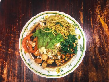 Ahşap masada kasede servis edilen sebze ve deniz ürünleri ile Asya yemeği.