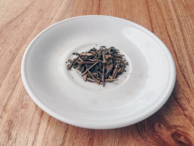 Tahta arka planda beyaz tabakta bitki çayı.