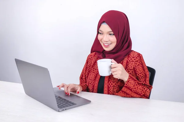 美しい若いアジアのイスラム教徒の女性は 白い部屋に座ってコーヒーを飲みながらラップトップコンピュータで作業を楽しんでいます — ストック写真