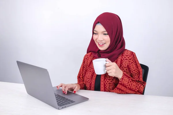 Beautiful Young Asian Islam woman is enjoy working on laptop computer while sitting at the white room, drinking coffee.