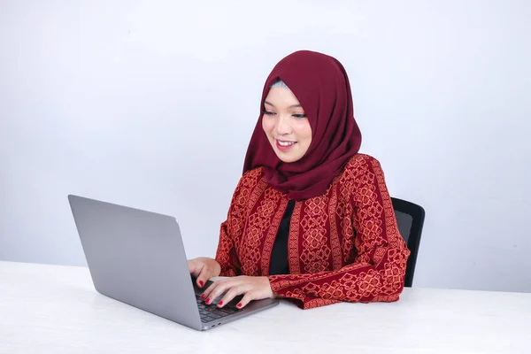 年轻的亚洲伊斯兰女性在白色背景的笔记本电脑上工作时 正坐在那里享受着微笑 — 图库照片