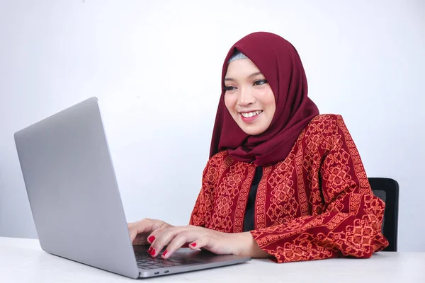 Genç Asyalı İslam kadını beyaz arka planda dizüstü bilgisayarla çalışırken eğleniyor ve gülümsüyor..