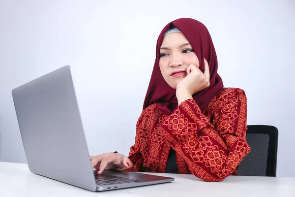 若いアジアのイスラム教徒の女性は ノートパソコンの前で顔に思考ジェスチャーの手で真剣に見ています — ストック写真