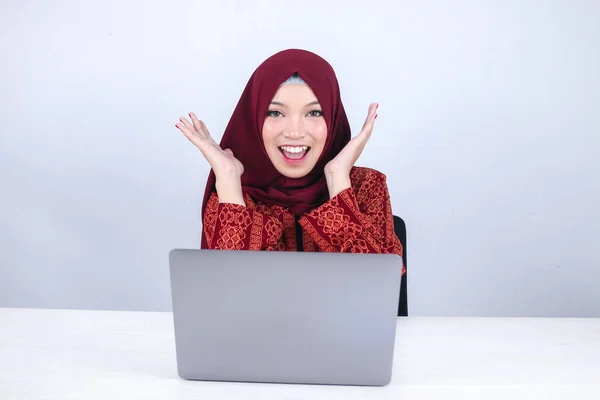 Young Asian Islam woman wearing headscarf is shocked and excited with what she see on laptop on the table.