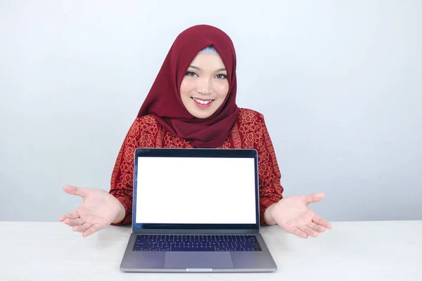 若いアジアのイスラム教徒の女性はカメラにノートパソコンの白いブランクスクリーンに指して見せて笑っています — ストック写真