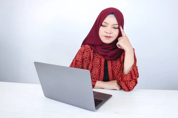 Young Asian Islam woman is smiling face with thinking gesture looking on the blank space in the front of laptop