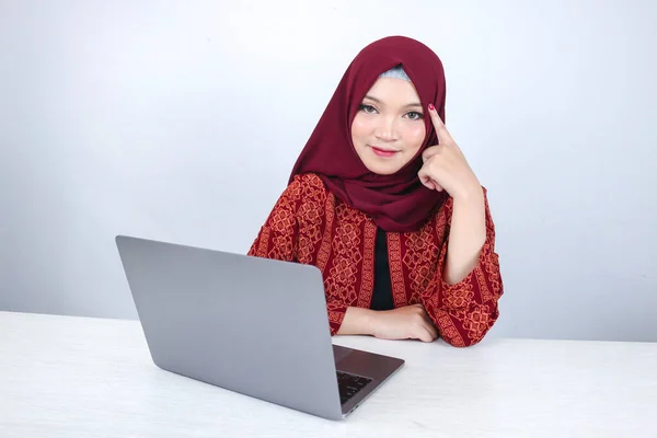 若いアジアのイスラム教徒の女性は ラップトップの前の空白のスペースを見て思考ジェスチャーで顔を笑っています — ストック写真