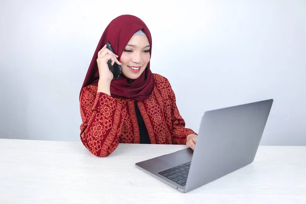 スカーフを被った若いアジア系イスラム教徒の女性は テーブルの上のノートパソコンで電話をかけると笑顔で興奮しています — ストック写真
