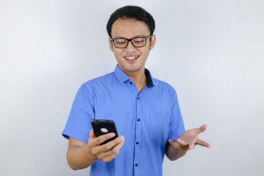 Elinde telefon olan Asyalı genç adamın gülümsemesi ve mutlu yüzü. Mavi gömlekli reklam modeli kavramı.