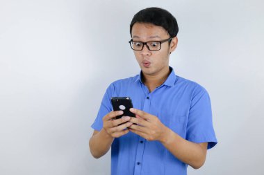 Genç Asyalı adam akıllı telefona baktığında şok olur ve mutlu olur.