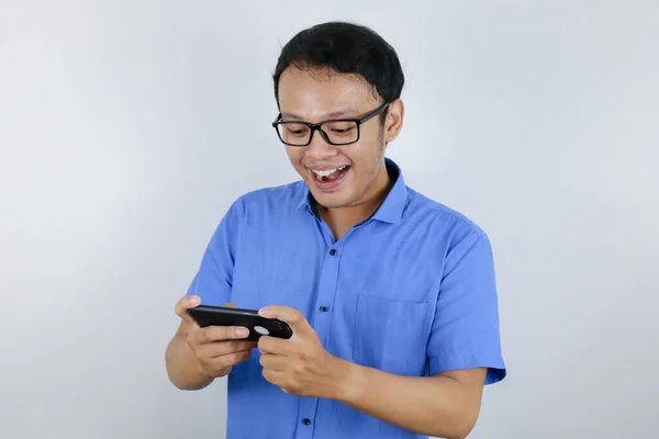 アジアの若者は ゲームをするときにスマートフォンで楽しさと笑顔 青いシャツを着たインドネシア人男性 — ストック写真
