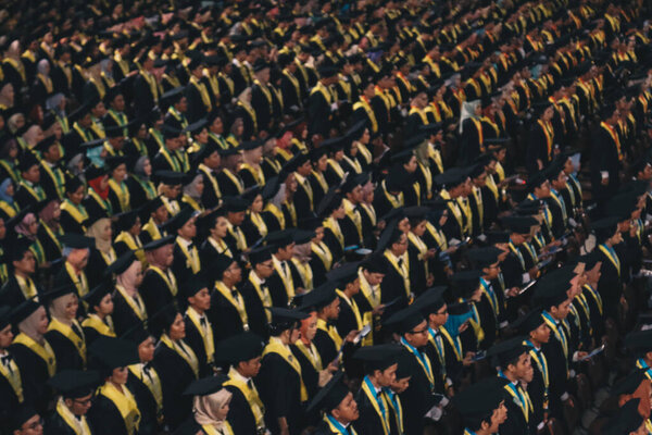 Top view of group of university graduates in black gowns lines up for degree in university graduation ceremony. Yogyakarta, Indonesia - December 2019.