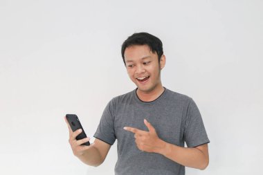 Gri tişörtlü Asyalı genç adam akıllı telefondan şaşırdı..