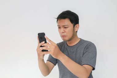 Genç Asyalı adam akıllı telefona baktığında ağlar ve üzülür. Endonezyalı adam siyah gömlek giyer. Gri arka plan..