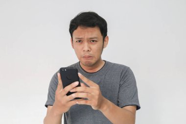 Genç Asyalı adam akıllı telefona baktığında ağlar ve üzülür. Endonezyalı adam siyah gömlek giyer. Gri arka plan..
