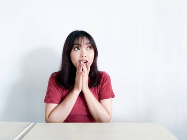 Genç Asyalı kadın, beyaz arka planda izole bir şekilde yukarılara bakarak jest yapmayı düşünüyor.