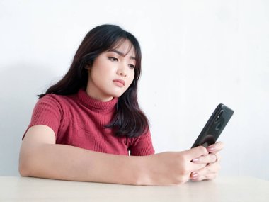 Asyalı güzel kız, izole edilmiş beyaz arka plandaki akıllı telefondan dışa bakıp düşünür ve yansıtır.