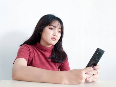 Asyalı güzel kız, izole edilmiş beyaz arka plandaki akıllı telefondan dışa bakıp düşünür ve yansıtır.