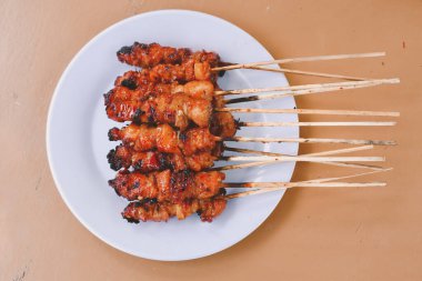Tavuk satay ya da tavuk derisi satay beyaz tabakta kırmızı baharat ile ahşap masalarda izole